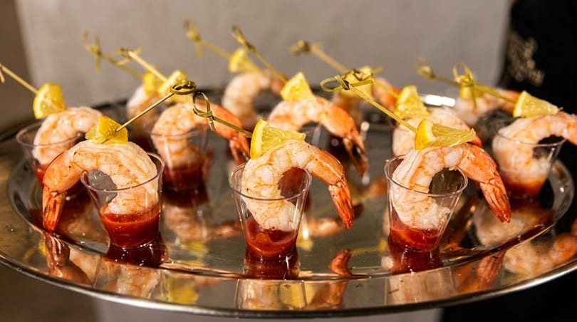 Shrimp cocktail appetizers with lemon wedges and sauce in small glasses on a silver tray.