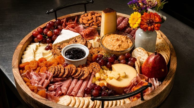 A large wooden charcuterie board filled with cheeses, meats, crackers, fruits, nuts, and dips.