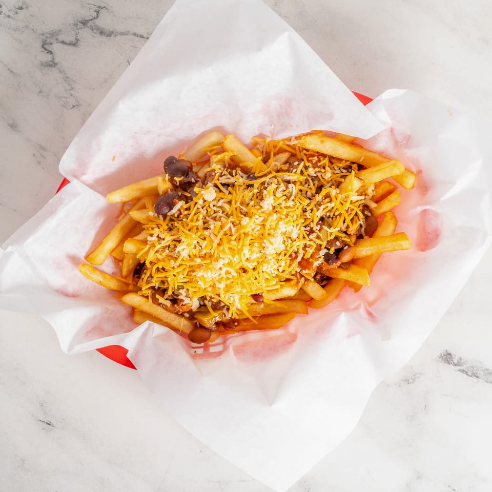 Loaded fries topped with chili, beans, shredded cheddar, and white cheese served on paper.