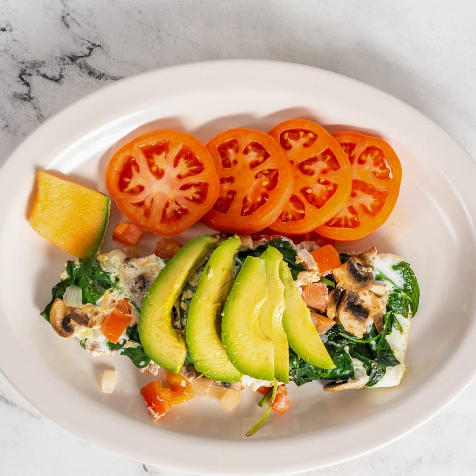 Plate of scrambled eggs with spinach, mushrooms, tomatoes, avocado slices, and a lime wedge.