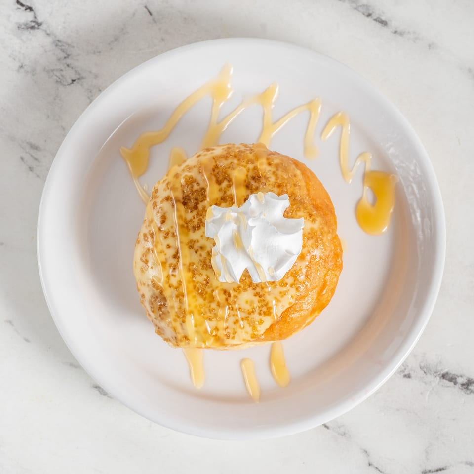 Golden-brown pancake topped with whipped cream and drizzled with syrup on a white plate.