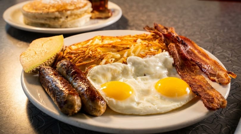 A diner breakfast plate with two eggs, hash browns, bacon, sausages, and a side of melon.