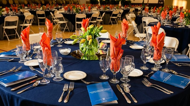 Tables set with blue tablecloths, orange napkins, and tulip centerpieces for a formal event.