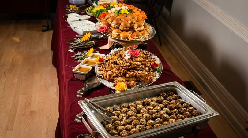 A buffet table laden with sliders, chicken skewers, meatballs, vegetable platter, and dips.