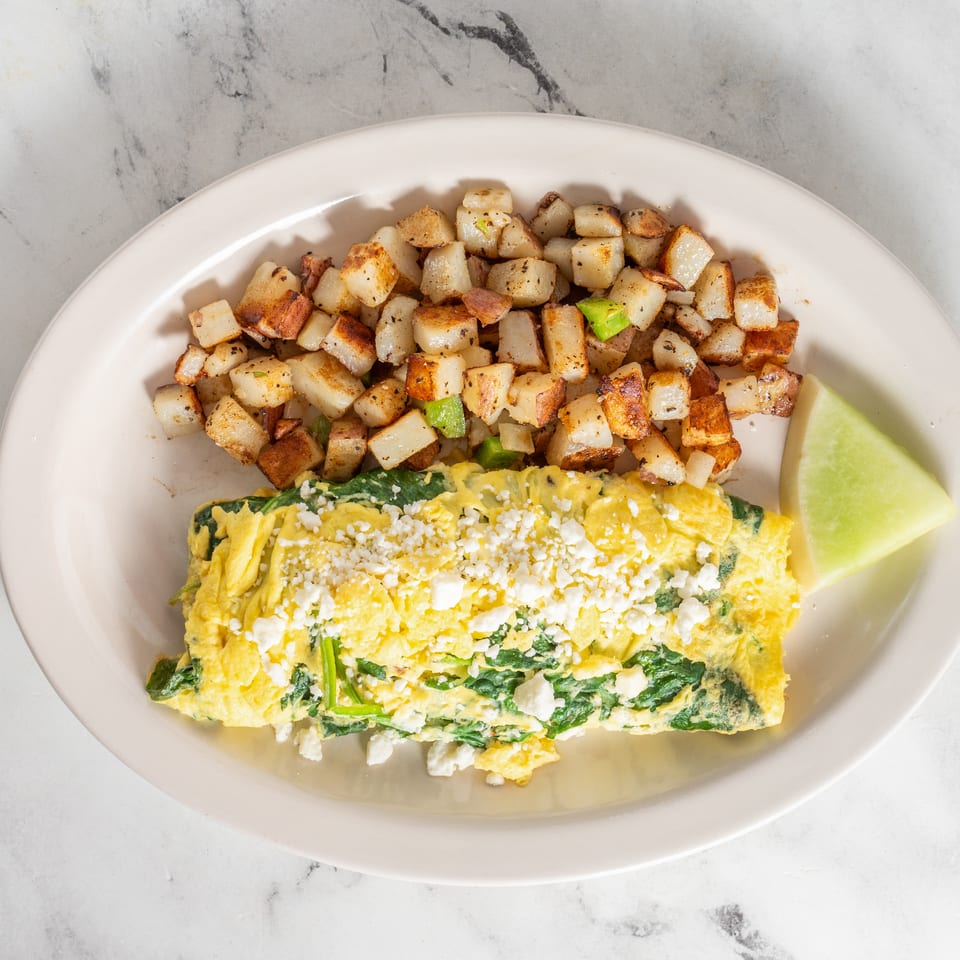 Spinach and feta omelet served with seasoned diced potatoes and a lime wedge on a white plate.