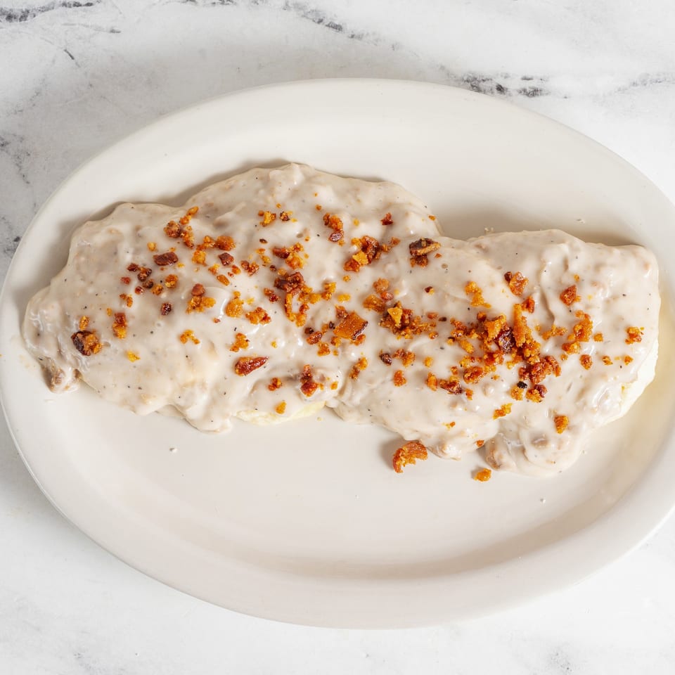 Creamy white-sauce pasta topped with crispy golden bacon pieces on a white oval plate.