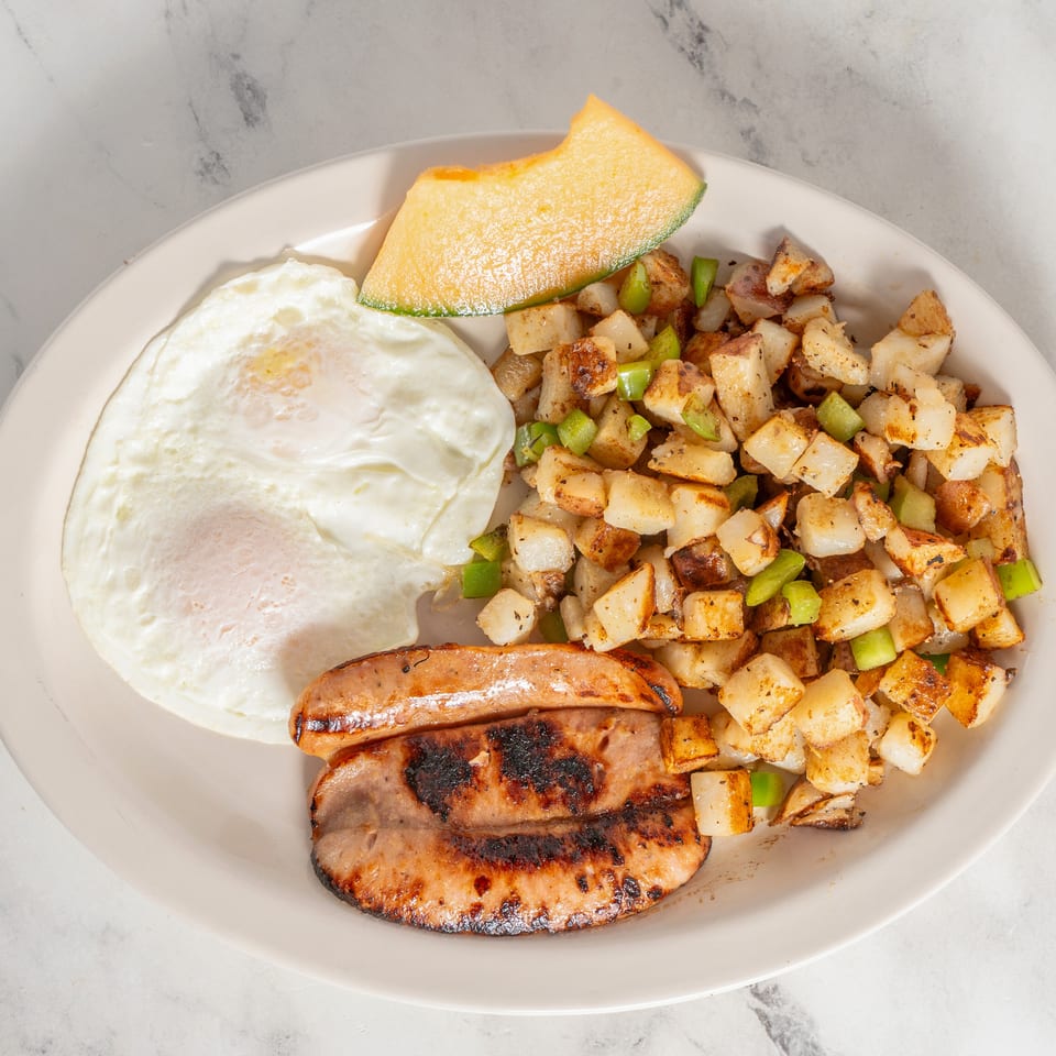 Breakfast plate with grilled sausage, two fried eggs, diced potatoes with green peppers, and a cantaloupe wedge.