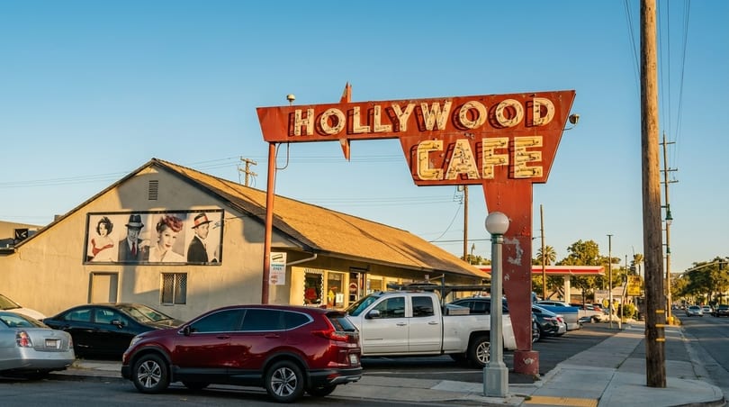Vintage Hollywood Cafe sign with classic movie star murals on the building, cars parked outside.