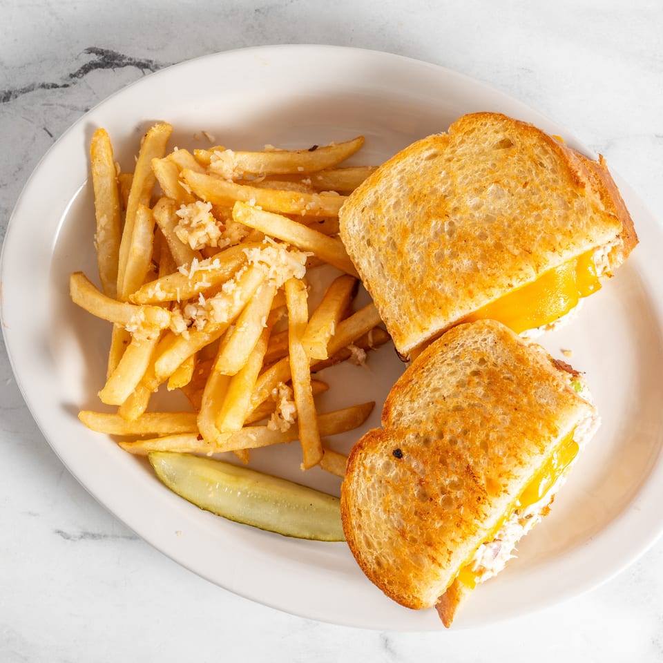 Grilled cheese sandwiches with melted cheddar, garlic fries, and a pickle spear on a white plate.