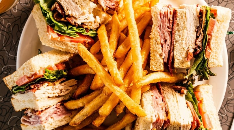 A close-up of a large plate filled with club sandwiches and golden french fries.