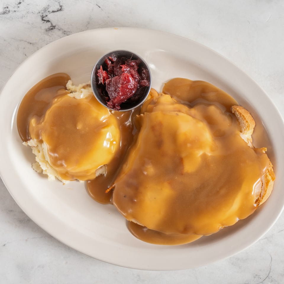Open-faced turkey sandwiches covered in gravy with mashed potatoes and cranberry sauce on a white plate.