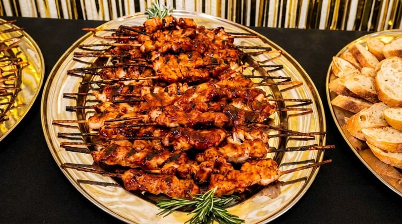 Platter of grilled chicken skewers with barbecue sauce and rosemary, next to sliced bread.