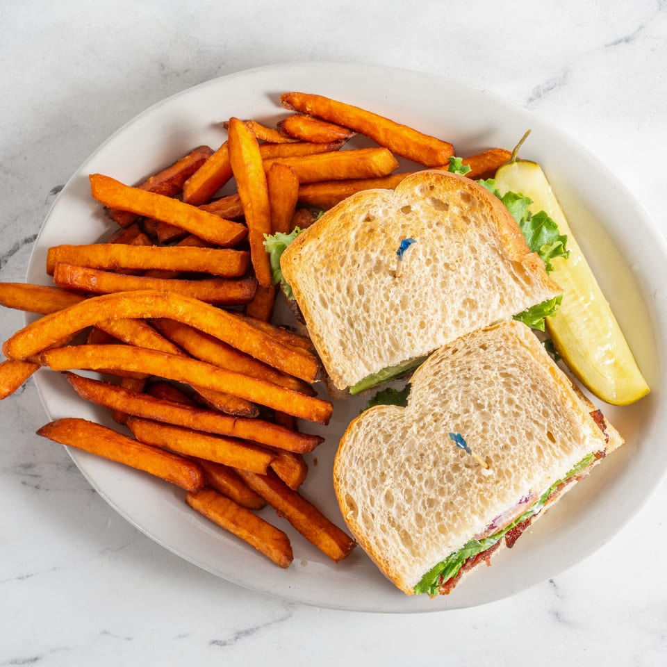 Plate of toasted sandwiches with lettuce and bacon, served alongside crispy sweet potato fries and a pickle spear.