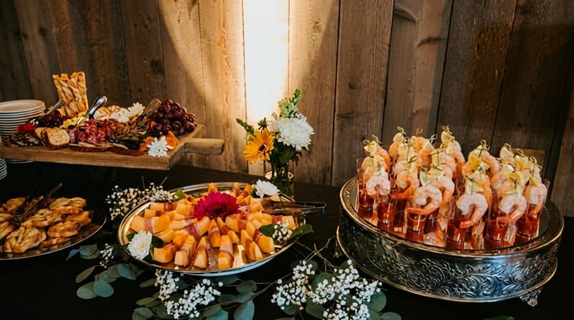 A buffet table with charcuterie, prosciutto-wrapped melon, shrimp cocktail, and pastries.