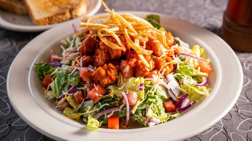 Crispy chicken salad with lettuce, tomatoes, red onion, shredded cheese, and tortilla strips.