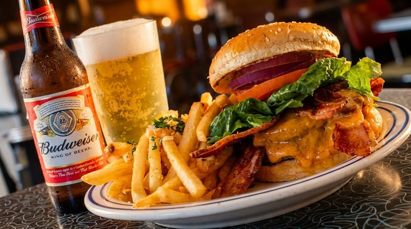 A juicy bacon cheeseburger with fries and a Budweiser beer bottle and glass.