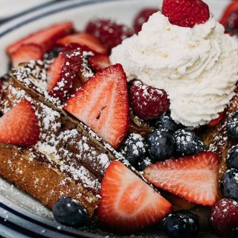 Golden waffles topped with fresh strawberries, blueberries, raspberries, powdered sugar, and whipped cream.