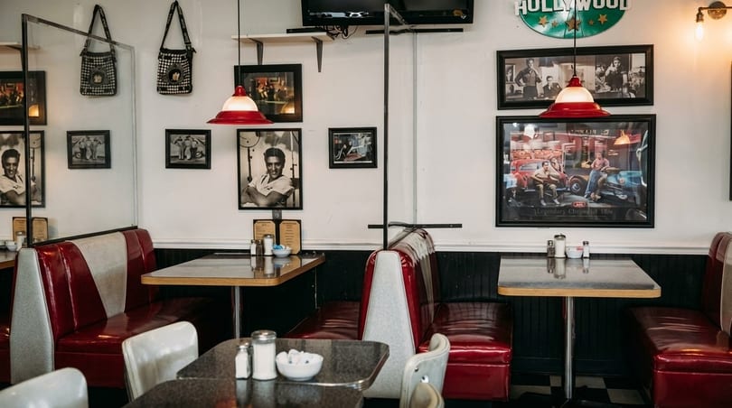 Retro diner interior with red and white booths, black and white checkered floor, and Elvis Presley pictures.