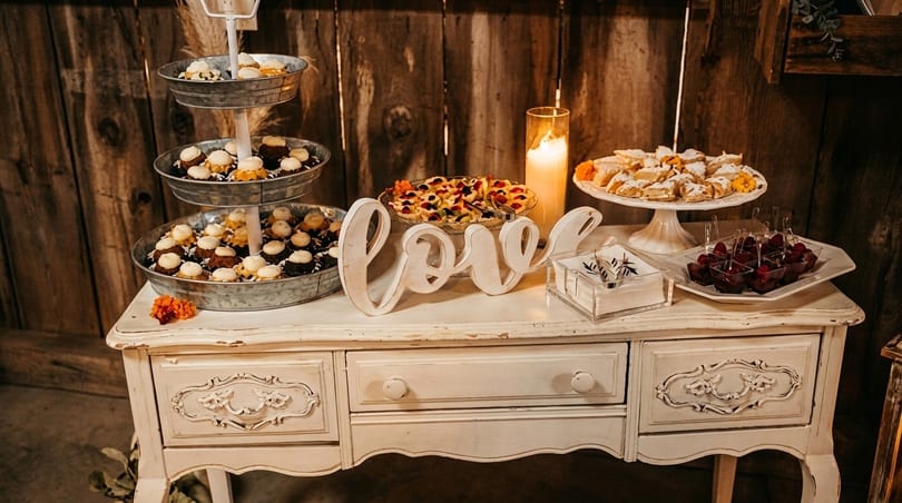 A rustic dessert table with cupcakes, fruit tarts, pastries, and raspberry parfaits, with a "Love" sign.