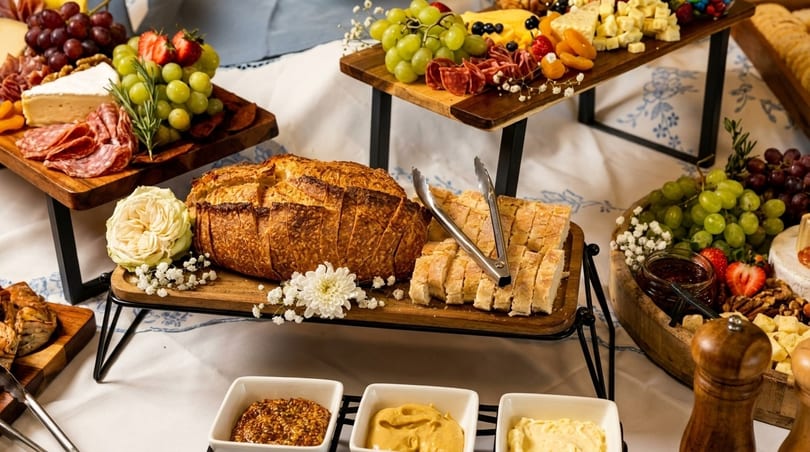 A buffet spread with charcuterie boards, artisan bread, and various condiments on a white tablecloth.