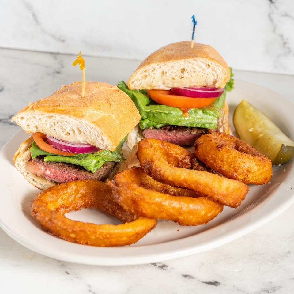 Two burgers with lettuce, tomato, onion, and grilled patties served with crispy fries and a pickle wedge on a plate.