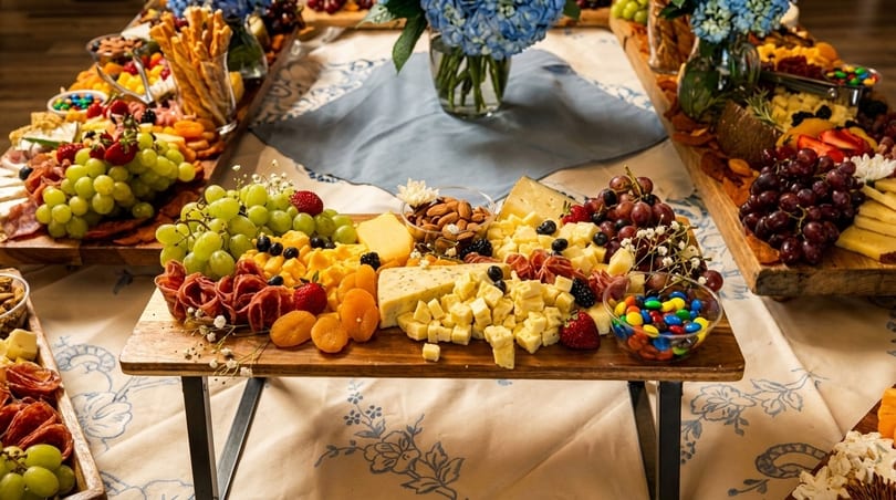 A long table filled with multiple charcuterie boards featuring cheeses, fruits, nuts, and candies.