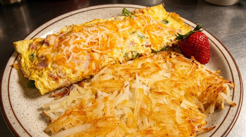 A cheese omelet with hash browns and a strawberry on a speckled plate.