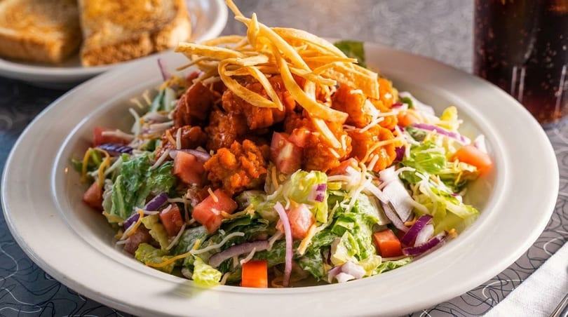 A large salad with crispy chicken, lettuce, tomatoes, cheese, and tortilla strips.