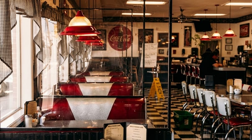 Interior of a retro diner with red booths, checkered floor, and a Coca-Cola sign.