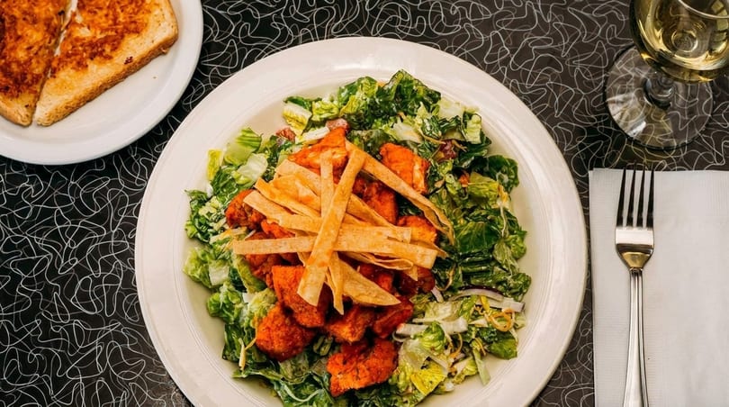Overhead view of a large salad with crispy chicken and tortilla strips, with garlic bread and wine.