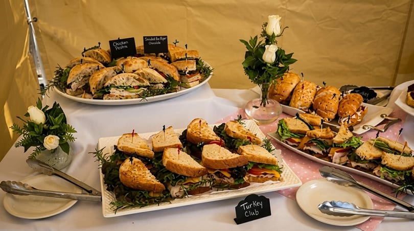 A buffet table with three platters of sandwiches, including chicken pesto and turkey club.